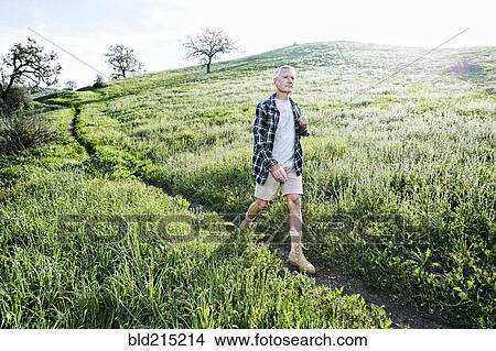 Picture - Older Caucasian man walking on dirt path. Fotosearch