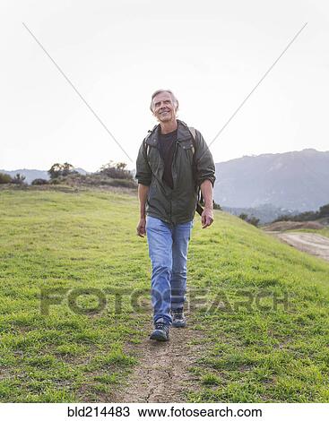 Stock Image - Older Caucasian man walking on dirt trail. Fotosearch
