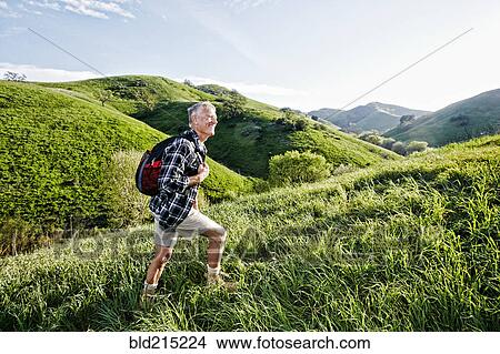 Picture - Older Caucasian man walking on grassy hillside. Fotosearch