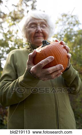 Stock Image - Older Caucasian woman admiring pumpkin outdoors. Fotosearch