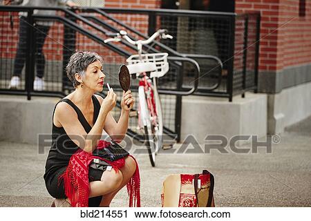 Older Caucasian woman applying makeup in mirror on sidewalk View Large Photo Image Stock Image - Older Caucasian woman applying makeup in mirror on sidewalk. Fotosearch