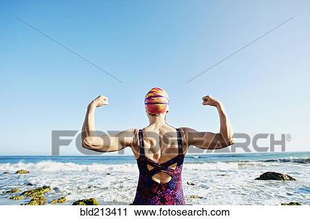 Stock Image - Older Caucasian woman flexing her muscles on beach. Fotosearch