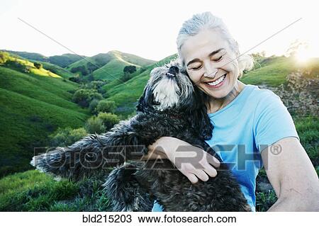 Stock Image - Older Caucasian woman hugging dog on rural hilltop. Fotosearch