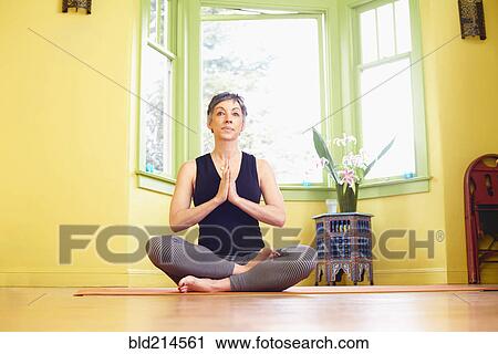 Stock Image - Older Caucasian woman meditating near window. Fotosearch
