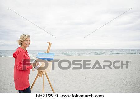 Stock Photo - Older Caucasian woman painting on beach. Fotosearch