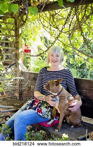 Picture - Older Caucasian woman petting dog in garden. Fotosearch