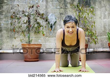 Stock Photography - Older Caucasian woman practicing yoga in courtyard. Fotosearch