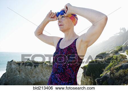 Stock Photograph - Older Caucasian woman putting on goggles on beach. Fotosearch