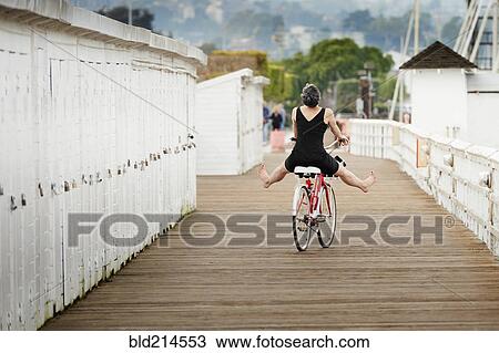 Stock Image - Older Caucasian woman riding bicycle on wooden dock. Fotosearch