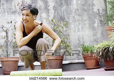 Stock Photograph - Older Caucasian woman rolling up yoga mat in courtyard. Fotosearch