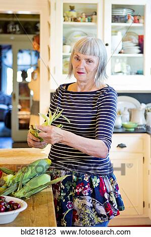 Stock Image - Older Caucasian woman shucking corn in kitchen. Fotosearch
