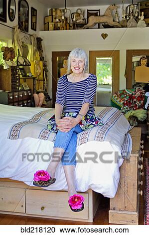 Stock Image - Older Caucasian woman sitting on bed. Fotosearch