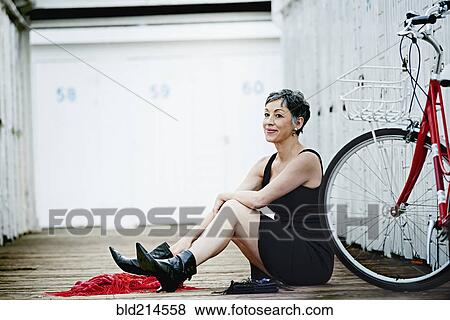 Stock Photo - Older Caucasian woman sitting with bicycle on wooden dock. Fotosearch