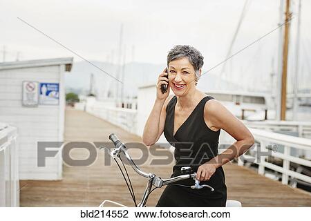 Stock Image - Older Caucasian woman talking on cell phone with bicycle. Fotosearch