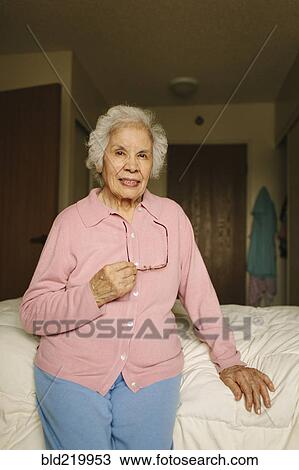 Stock Image - Older mixed race woman sitting on bed. Fotosearch