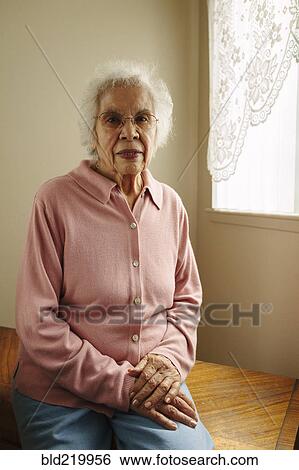 Stock Photograph - Older mixed race woman sitting on table. Fotosearch
