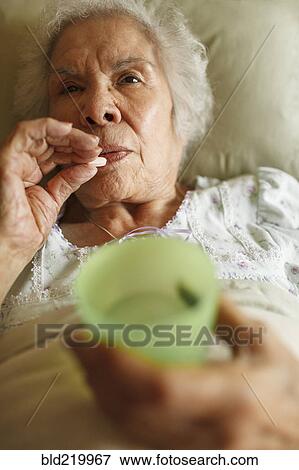 Stock Photo - Older mixed race woman taking medication in bed. Fotosearch
