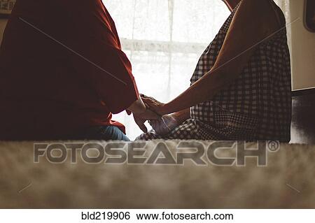Older woman holding hand of daughter on bed View Large Photo Image Stock Photograph - Older woman holding hand of daughter on bed. Fotosearch