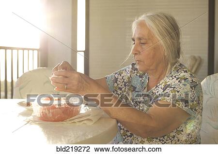 Stock Image - Older woman peeling fruit at table. Fotosearch
