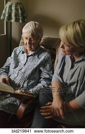 Stock Image - Older woman reading to granddaughter in living room. Fotosearch