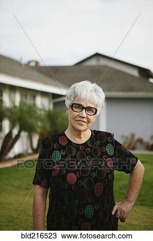 Stock Image - Older woman standing with hands on hips in backyard. Fotosearch