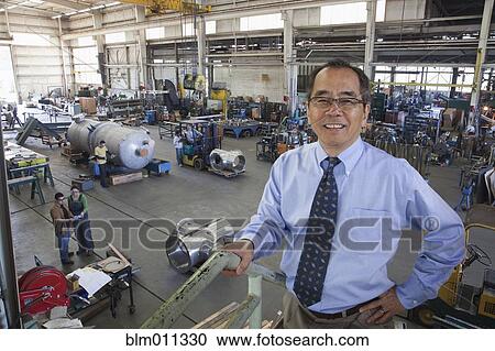 Stock Image - Pacific Islander businessman standing in factory. Fotosearch