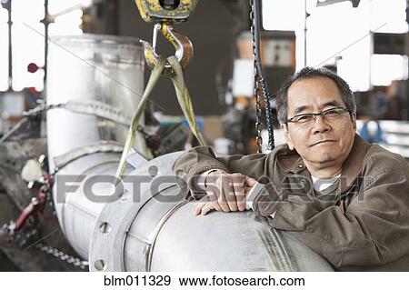 Stock Photo - Pacific Islander leaning on pipe in factory. Fotosearch