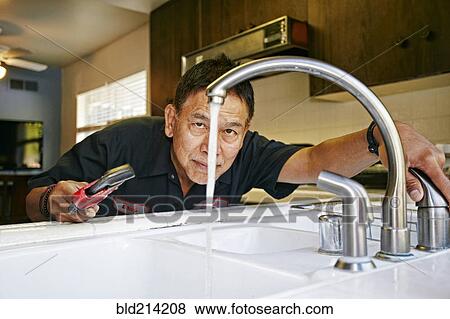 Stock Photo - Pacific Islander plumber examining sink in kitchen. Fotosearch