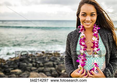 Stock Photo - Pacific Islander woman wearing flower lei near rocky beach. Fotosearch