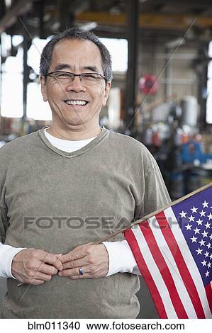 Stock Image - Pacific Islander worker holding American flag. Fotosearch