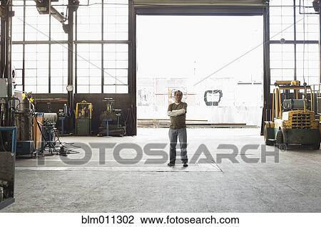 Stock Image - Pacific Islander worker standing in warehouse. Fotosearch