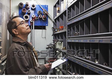 Stock Photo - Pacific Islander worker writing on clipboard. Fotosearch