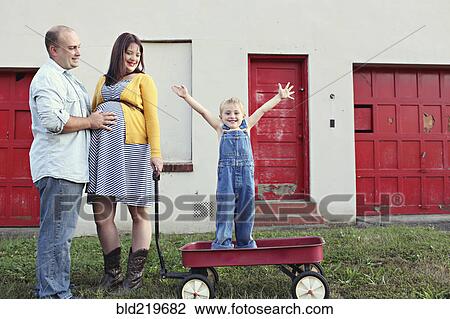 Stock Image - Parents watching son cheering in toy wagon. Fotosearch