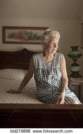 Stock Photo - Pensive older woman sitting on bed. Fotosearch
