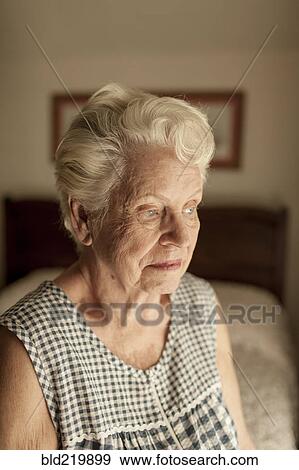 Stock Photo - Pensive older woman sitting on bed. Fotosearch