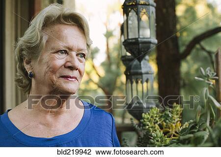 Stock Image - Pensive older woman standing on porch. Fotosearch