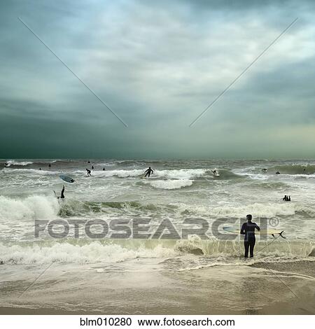 Stock Image - People surfing in stormy ocean. Fotosearch