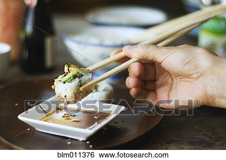 Stock Photograph - Person eating sushi with chopsticks. Fotosearch