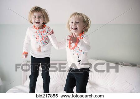 Stock Photography - Playful sisters jumping on bed. Fotosearch