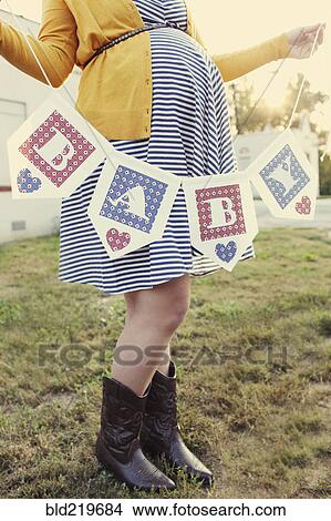 Picture - Pregnant Caucasian woman holding baby banner in backyard. Fotosearch