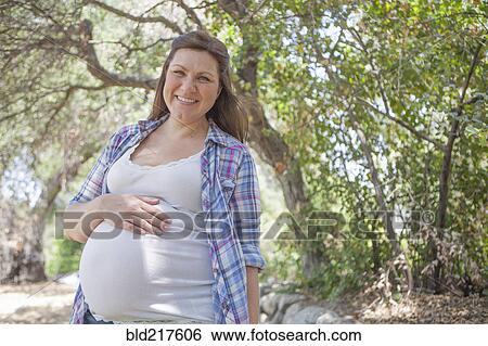 Stock Photograph - Pregnant Caucasian woman standing in park. Fotosearch