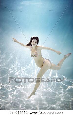 Stock Image - Pregnant Caucasian woman swimming underwater. Fotosearch