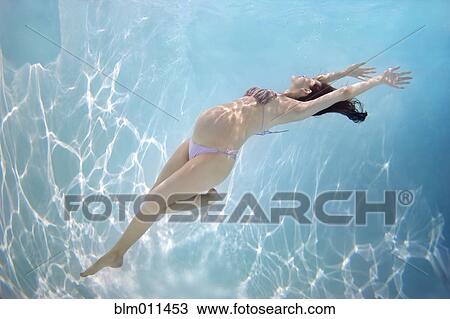 Stock Image - Pregnant Caucasian woman swimming underwater. Fotosearch