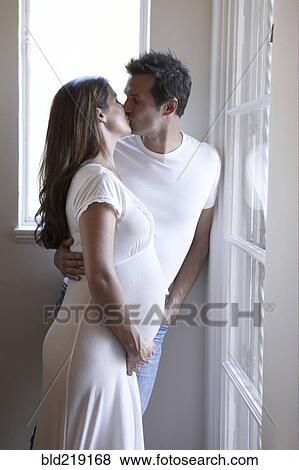 Stock Photo - Pregnant couple kissing at window. Fotosearch