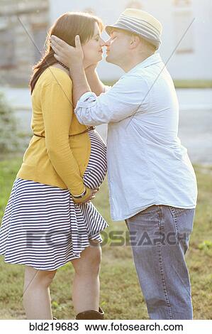 Stock Image - Pregnant couple kissing in sunny field. Fotosearch