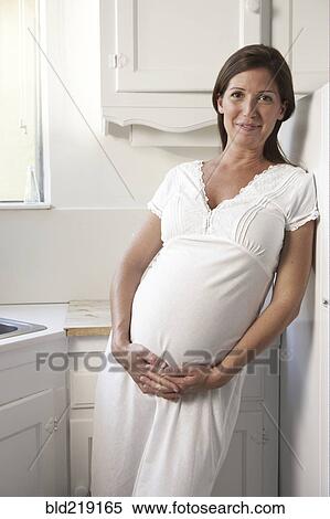 Stock Photography - Pregnant woman holding her belly in kitchen. Fotosearch