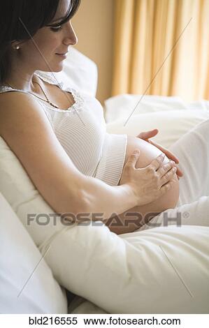 Pregnant woman rubbing her belly on sofa View Large Photo Image Stock Photography - Pregnant woman rubbing her belly on sofa. Fotosearch