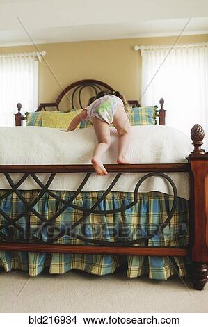 Picture - Rear view of baby girl climbing bed. Fotosearch