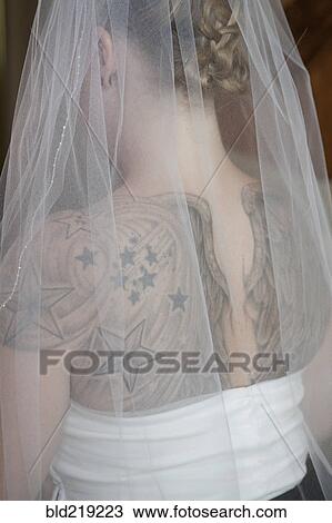 Stock Image - Rear view of Caucasian bride in veil with tattoos on back. Fotosearch