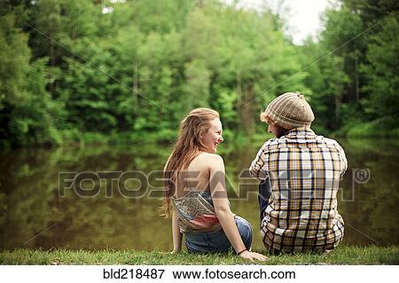 Stock Photo - Rear view of couple sitting near lake. Fotosearch